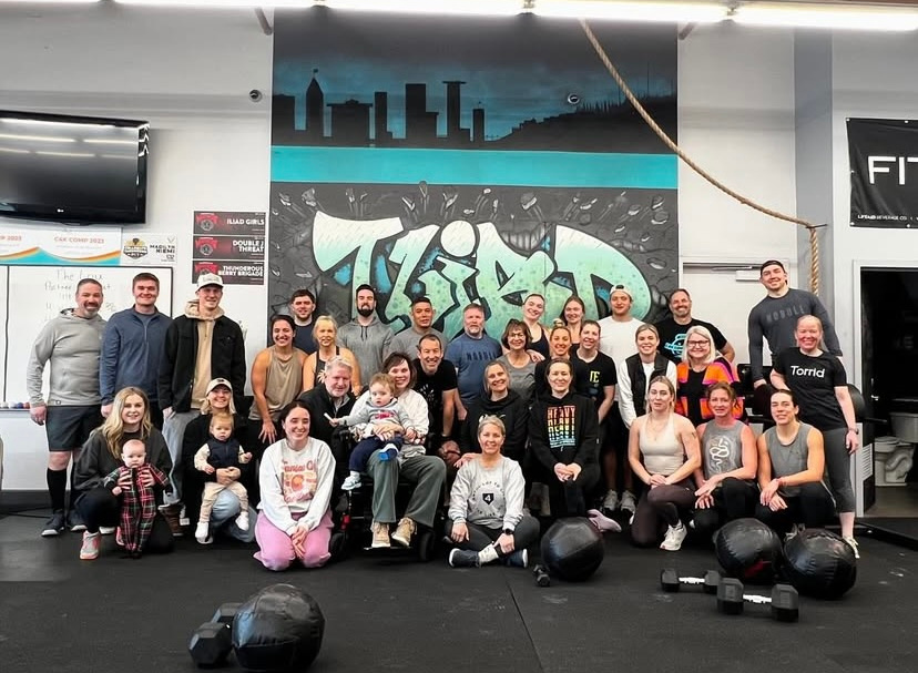 A large group of adults and children pose together in a gym.