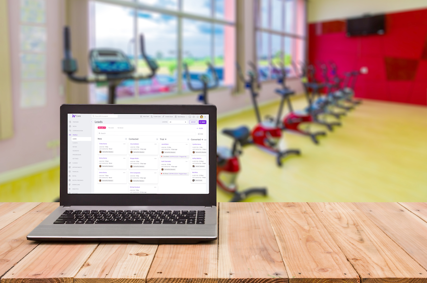 A laptop displaying the Wodify Leads interface sits on a wooden table in the gym.